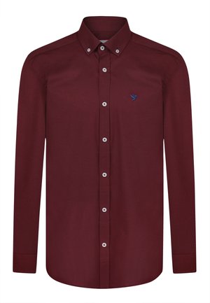 Camisa de manga larga color burdeos con cuello abotonado, presenta botones blancos y un logo de un pájaro azul en el lado izquierdo. Textura de tela suave.
