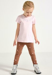 Lyserød bomuld T-shirt med blomsterbroderi, kombineret med brune leggings med lyserøde sommerfuglemønstre og sølvfarvede ankelstøvler.
