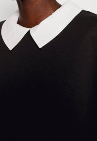 Indumento nero con una texture morbida presenta un colletto classico bianco a contrasto. Il colletto ha una forma arrotondata ed è cucito con cura.