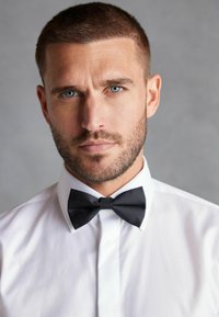 Cămașă albă cu cravat�ă neagră, având un guler clasic și o textură netedă. Detalii remarcabile includ o croială curată și ajustată.