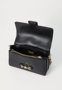Borsa in pelle nera con cerniera e dettagli dorati, caratterizzata da un design aperto. L'interno presenta un'etichetta del marchio e una texture liscia.
