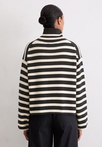 Gestreifter Pullover mit hohem Kragen und langen Ärmeln, der abwechselnd schwarze und cremefarbene horizontale Streifen, eine gerippte Textur und eine lässige Passform aufweist.