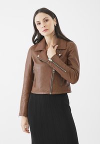 Giacca cropped in pelle marrone con zip argentate, ampio colletto e tasche laterali con zip. Indossata sopra una gonna plissettata nera.