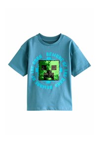 Turkis bomulds T-shirt med et pixeliseret grønt ansigt med sort omrids og teksten "VÆR OPSØGELIG FOR DET MØRKE" i blåt omkring det.