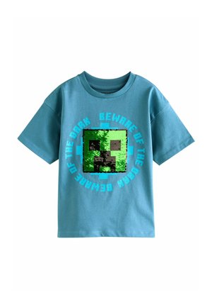 Turkos bomulls t-shirt med en pixeliserad grön ansiktsgrafik med svart kontur och texten "VAKTA DIG FÖR MÖRKRET" i blått runt om.