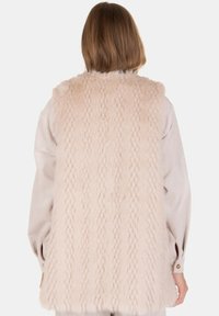 Chaleco de piel sintética en rosa pálido con un diseño texturizado de costillas verticales. Presenta un ajuste relajado y una apariencia suave y acogedora.