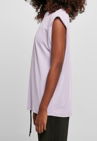 Fialový top s krátkým rukávem, uvolněného střihu, kulatým výstřihem a ohrnutými rukávy, vyrobený z měkké bavlny. Obsahuje tkaničky na lemu.