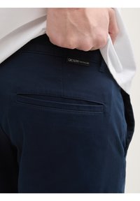 Marineblaue Denim-Hosen mit glatter Textur, ausgestattet mit einer Gesäßtasche, einem Etikett mit der Aufschrift "DENIM TOM TAILOR" und einem figurbetonten Design.