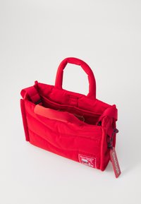 Sac en tissu matelassé rouge avec deux anses courtes, une bandoulière réglable, plusieurs poches et une étiquette avec le logo "Coachtopia".