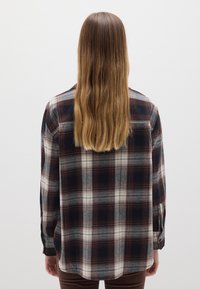 Flanellen overhemd in marineblauw, beige en bordeaux geruit. Heeft een losse pasvorm, lange mouwen en een zoom aan de achterkant. Zachte textuur.