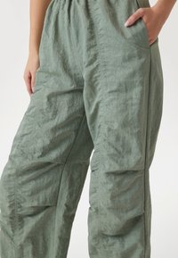 Pantaloni de culoare verde deschis, texturați, cu un tiv elastic strâns, buzunare laterale și croială lejeră, având un design din material plisat.
