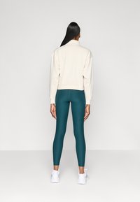 Sweatshirt branco cortado e leggings teal, com uma textura suave e ajustada, combinados com sapatos atletas brancos. Sem padrões ou detalhes visíveis.