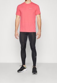 Červené atletické tričko s krátkým rukávem, černé fitted legíny a černé běžecké boty s bílým logem Nike. Jednoduchý design, lehký materiál.