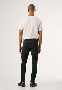 Tummansinisiä slim fit -farkkuja, jotka on yhdistetty vaaleanbeigeen T-paitaan, nähtynä takaa. Selkeä ompelu ja kaksi takataskua näkyvissä.