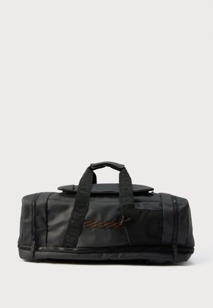 Sort duffel taske med dobbelte håndtag, front mesh-lomme, lynlåskomponenter og mærkede stropper på en ensartet lys baggrund.