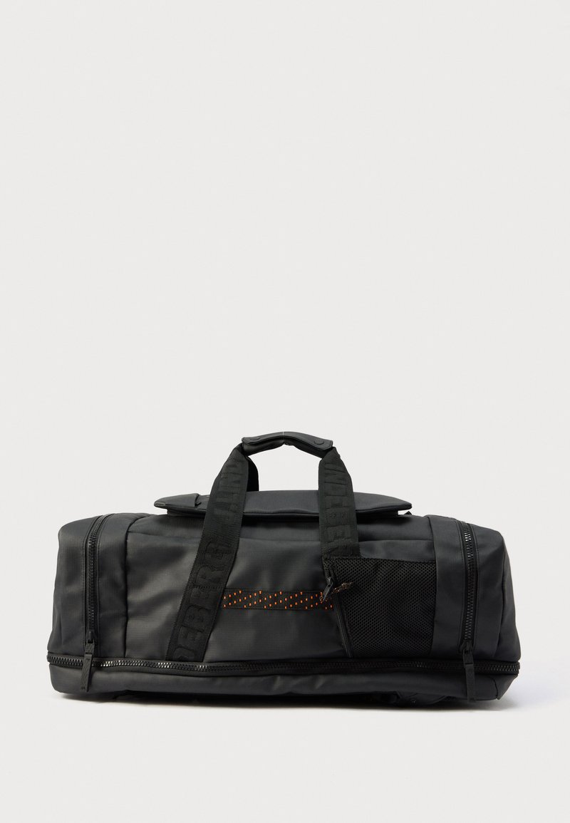 Μαύρη τσάντα τύπου duffel με διπλές λαβές, μπροστινή τσέπη από δίχτυ, διαμερίσματα με φερμουάρ και λουριά με επωνυμία σε απλό φωτεινό φόντο.