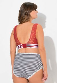 Punane pitsist bralette laiade rihmadega, millel on triibuline elastne vöö. Koos musta ja valge triibulise kõrge vöökohaga aluspükstega, millel on pitsäär.