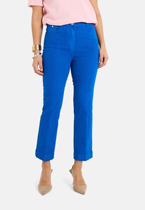 Pantalones azules brillantes de mezcla de algodón, con un corte slim, puños enrollados y diseño de cinco bolsillos. Combinados con una blusa rosa clara y tacones beige.