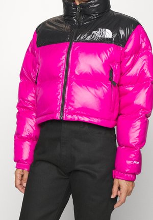 Bright pink and black cropped puffer jacket with front zipper and side pockets, featuring "The North Face" logo on the chest.