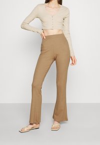 Beige kortärmad långärmad topp med knappar, i kombination med ljusbruna utsvängda byxor. Slät yta, åtsittande design och mjukt tyg.