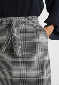 Pantaloni a scacchi bianco e nero con vita con cintura, dotati di tasche e tessuto testurizzato, con motivi a quadri visibili sulla superficie.