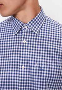 Blauwe en witte ruitjesoverhemd met een button-down kraag, een enkele borstzak en geborduurd logo. Heeft een gladde stof en knopen.