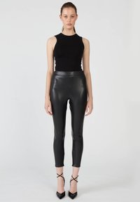 Czarny bezrękawnik zestawiony z czarnymi dopasowanymi skórzanymi legginsami, charakteryzującymi się wysokim stanem i zwężanym krojem sięgającym kostek.