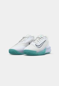 Chaussures de sport blanches avec dessus texturé, accents gris et semelle en caoutchouc teal. Présente un design élégant avec des lacets et un logo sur le côté.