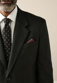 Black suit jacket with notch lapels, paired with a patterned black tie featuring paisley designs in orange and white. Maroon pocket square visible.