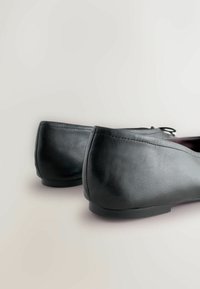 Zapatos de cuero negro con textura suave, tacón bajo y diseño de punta redondeada, con costuras mínimas y sin detalles visibles de herrajes.