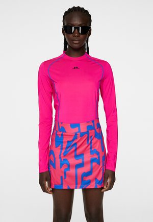Langsleeve roze top met blauwe stiksels, gecombineerd met een roze rok met een gedurfde blauwe abstracte patroon. De textuur is glad, het materiaal lijkt lichtgewicht.