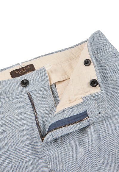 Light blue plaid pants with beige inner lining, black buttons, and partially open zipper revealing inside details and SLOWEAR brand label.