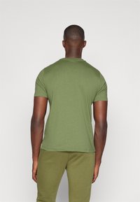 Ελαιοπράσινη κοντομάνικη μπλούζα από μαλακό βαμβακερό τζέρσεϊ, με κλασικό λαιμόκοψη και χαλαρή γραμμή, συνδυασμένη με παντελόνια ίδιου χρώματος.