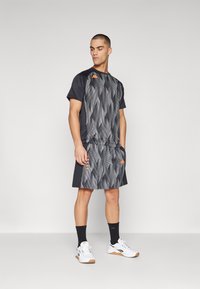 Sport outfit in gray featuring a patterned short-sleeve shirt and shorts. Accented with orange logos. Worn with dark socks and white sneakers.