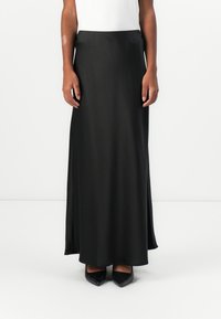 Schwarzer Satin-Maxikleid mit glatter Textur und seitlichen Schlitzen, kombiniert mit schwarzen spitzen Absatzschuhen. Gerader Taillenschnitt, keine sichtbaren Muster.