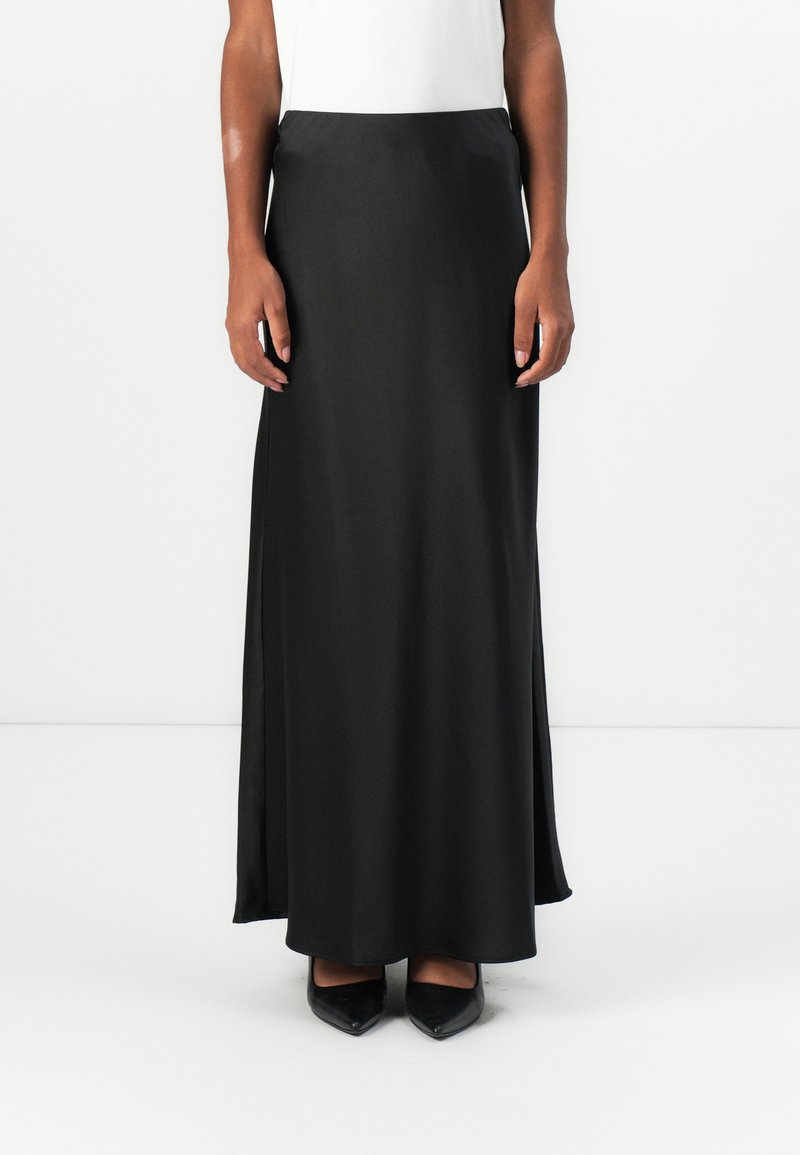 Schwarzer Satin-Maxikleid mit glatter Textur und seitlichen Schlitzen, kombiniert mit schwarzen spitzen Absatzschuhen. Gerader Taillenschnitt, keine sichtbaren Muster.