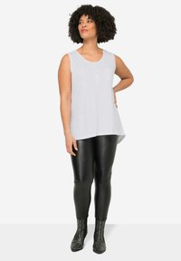 Top blanco sin mangas con escote redondo y tapeta de botones, combinado con leggings negros ajustados y botas de tobillo con tachuelas.