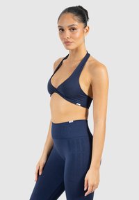 Marinblå sportbehå med en vriden frontdesign, tillsammans med högmidjade leggings med ett subtilt texturerat logomönster.