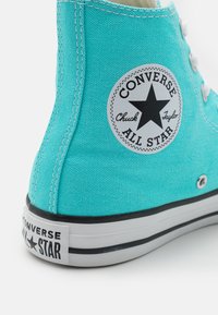 Sneaker alta in tela turchese con suola in gomma bianca, patch con logo a stella nera e dettagli in occhioletto argentato. Testo nero sul tallone.