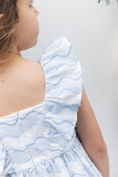 Φόρεμα σε μπλε και λευκό χρώμα με μανίκια με βολάν, διακοσμημένο με κυματιστό σχέδιο και φερμουάρ στο πίσω μέρος. Το υφασμάτινο ύφος προσθέτει διάσταση.