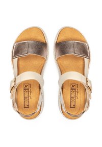 Sandalias ligeras con una correa metálica en bronce y una correa ajustable para el tobillo en color crema. Plantilla suave en marrón con bordes texturizados.