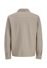Beige langærmet skjorte med krave, der har en struktureret stof, diskret sømdetaljering og sprækker ved manchetterne.