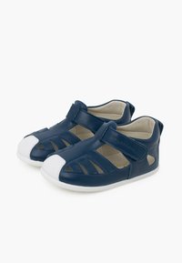 Sandales en cuir bleu marine avec un design découpé, embout blanc, et fermeture par bande Velcro. Comprend une doublure intérieure beige et une semelle blanche flexible.