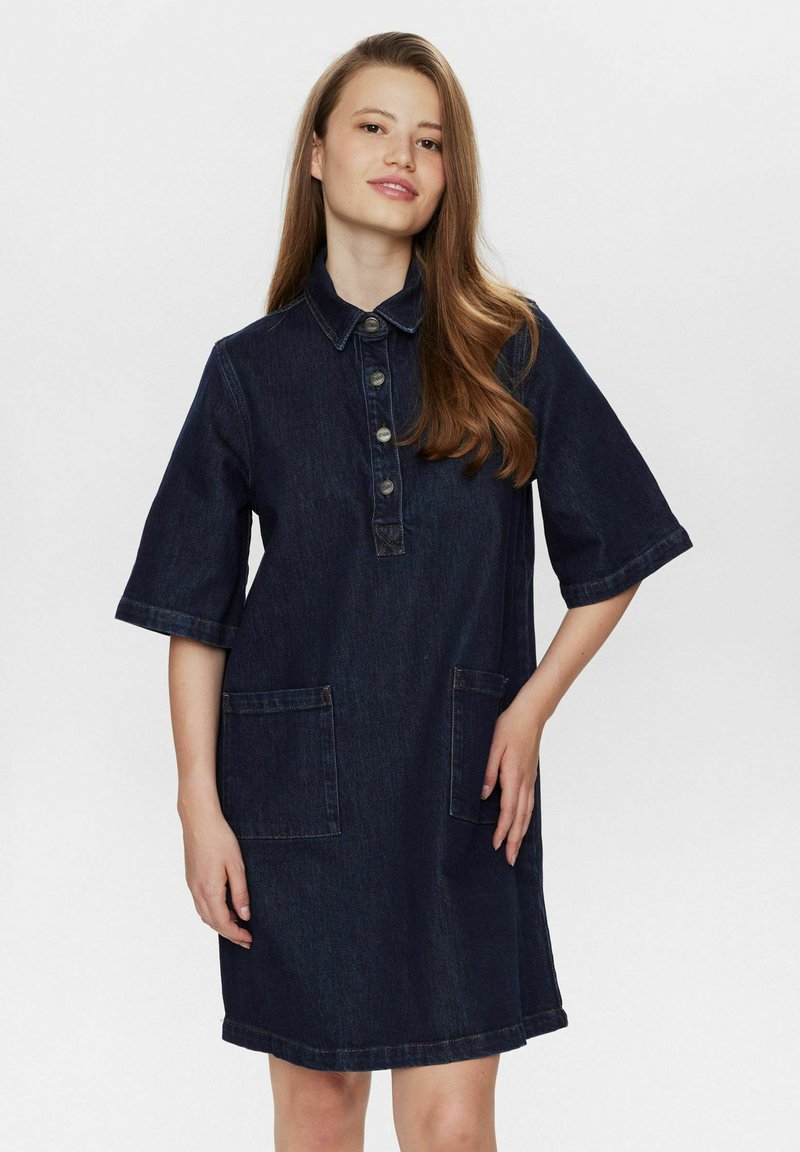 Denim jurk in donkerblauw, met een shirtkraag, knopen aan de voorkant, korte mouwen en twee voorzakken. Soepele textuur, relaxed fit.