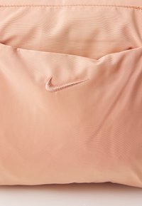 Nike pouch in zacht perzikachtig stof, met een subtiele glans en stiksel, voorzien van een geborduurd logo in een bijpassende kleur.