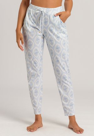 Kvinde iført lyseblå bukser med paisley-mønster og snøring, med lommer, barfodet, stående mod en ensfarvet baggrund.