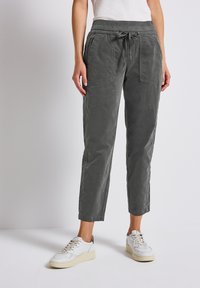 Grijze, taps toelopende stoffen broek met een elastische tailleband en trekkoord. Beschikt over twee grote frontzakken en een zachte, gekorrelde afwerking.