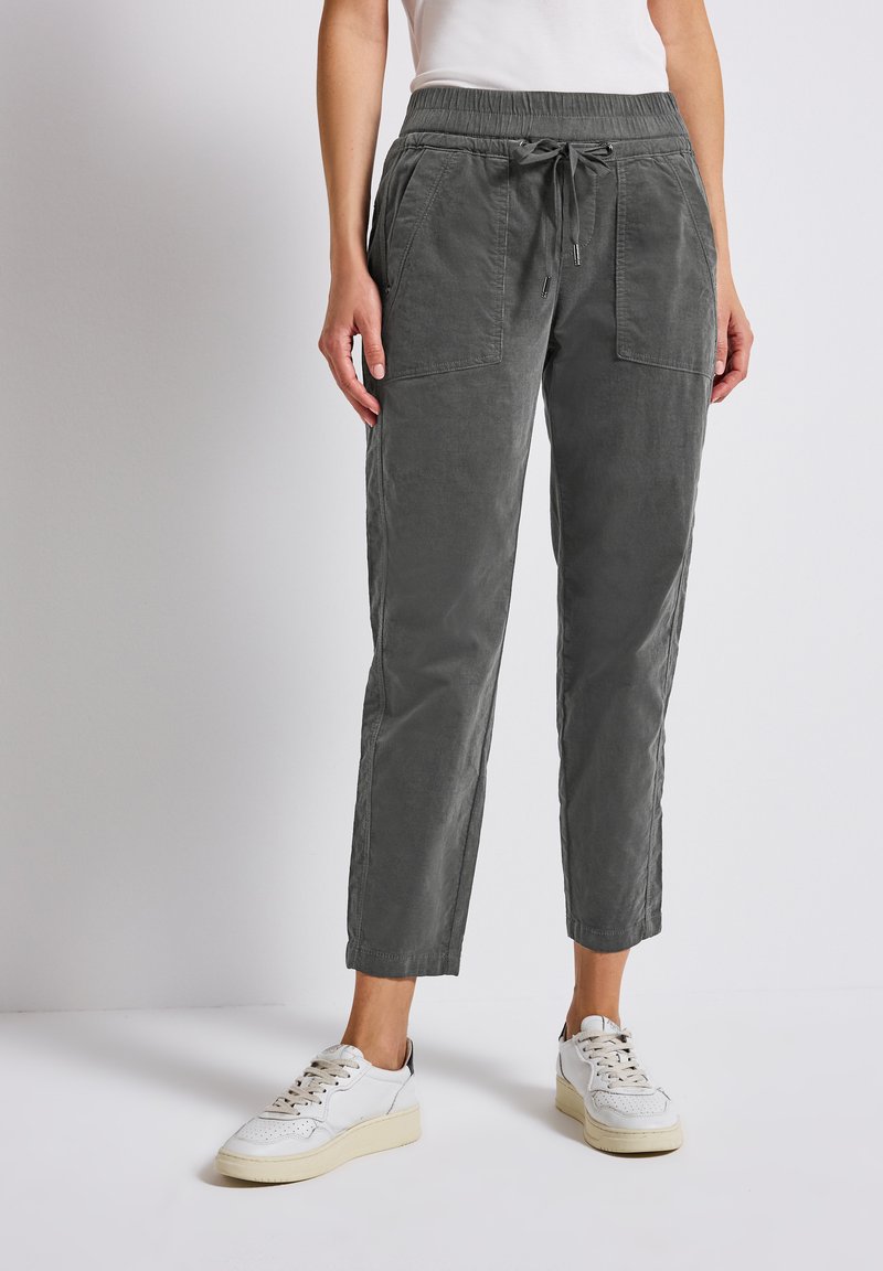 Grijze, taps toelopende stoffen broek met een elastische tailleband en trekkoord. Beschikt over twee grote frontzakken en een zachte, gekorrelde afwerking.