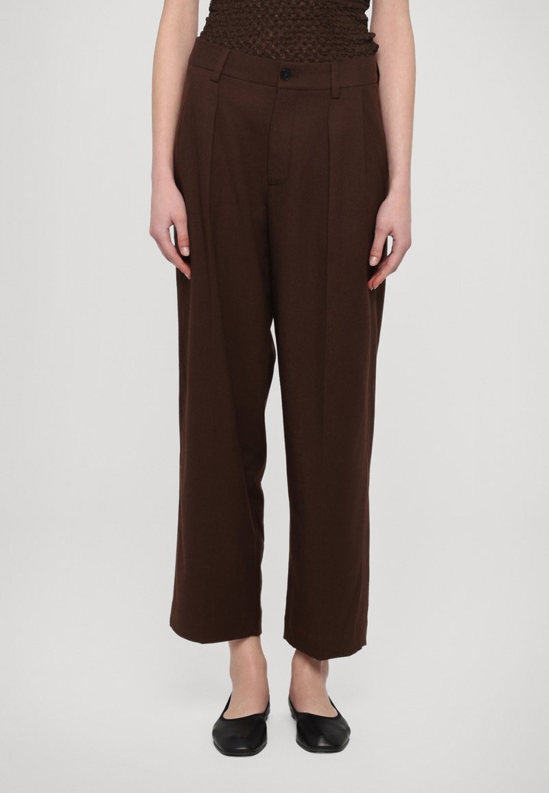 Brown wide-leg trousers with a high waist, featuring a single button closure, front pleats, and side pockets. Fabric appears smooth and soft.