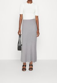 Falda maxi gris con ribetes y un ligero vuelo, combinada con una camiseta ajustada de manga corta blanca. Incluye sandalias negras elegantes y un bolso.